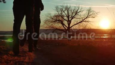夕阳下，路上两个人站在一棵树上剪影。 运动的年轻人在大自然中奔跑